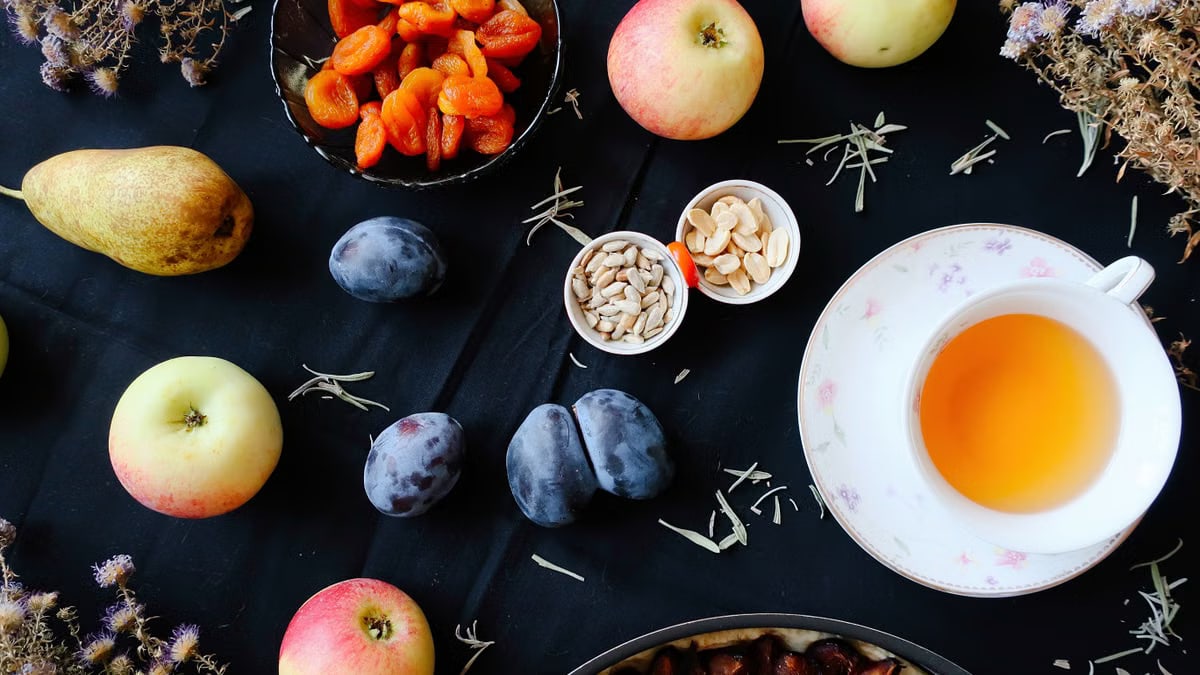 Cozy autumn flat lay with apples, plums, pears, and a warm cup of tea.